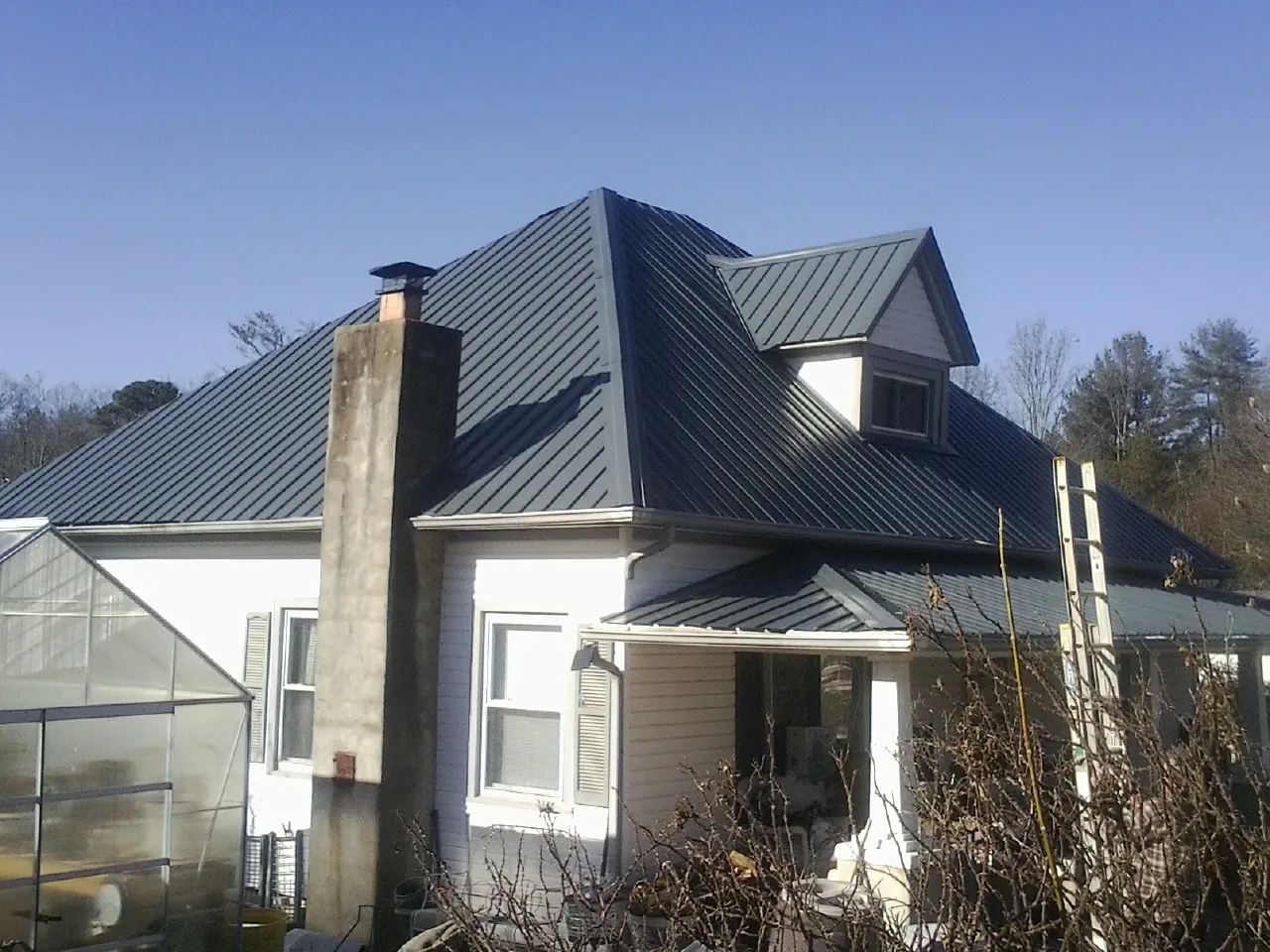 Dark blue standing seam metal roof on a white farmhouse with dormer — Slate & Tile Roof Repair by Roofing Brothers in Hockley