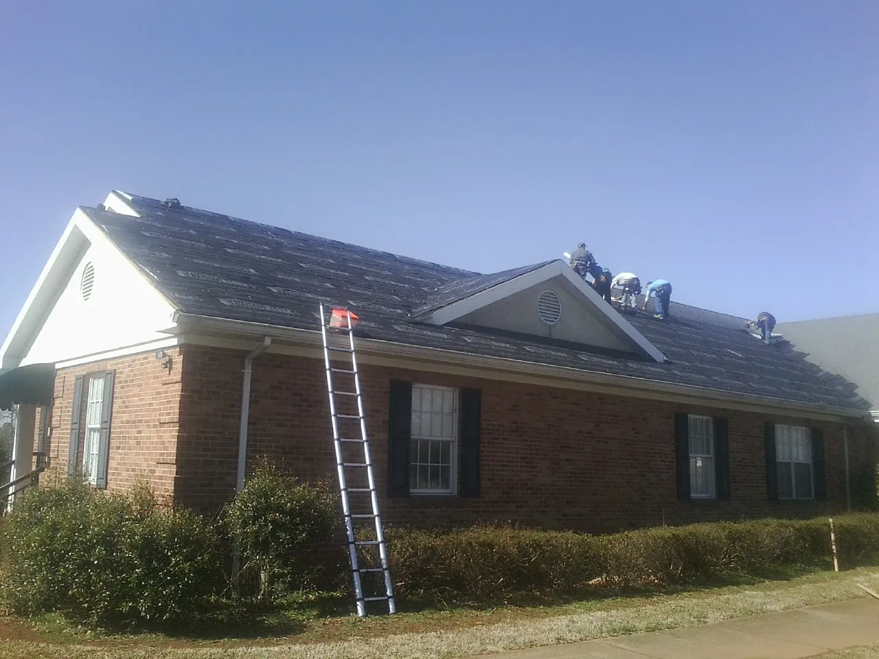 Crew tearing shingles off a brick ranch roof with a ladder set — Metal Roof Repair work by our crew in Hockley