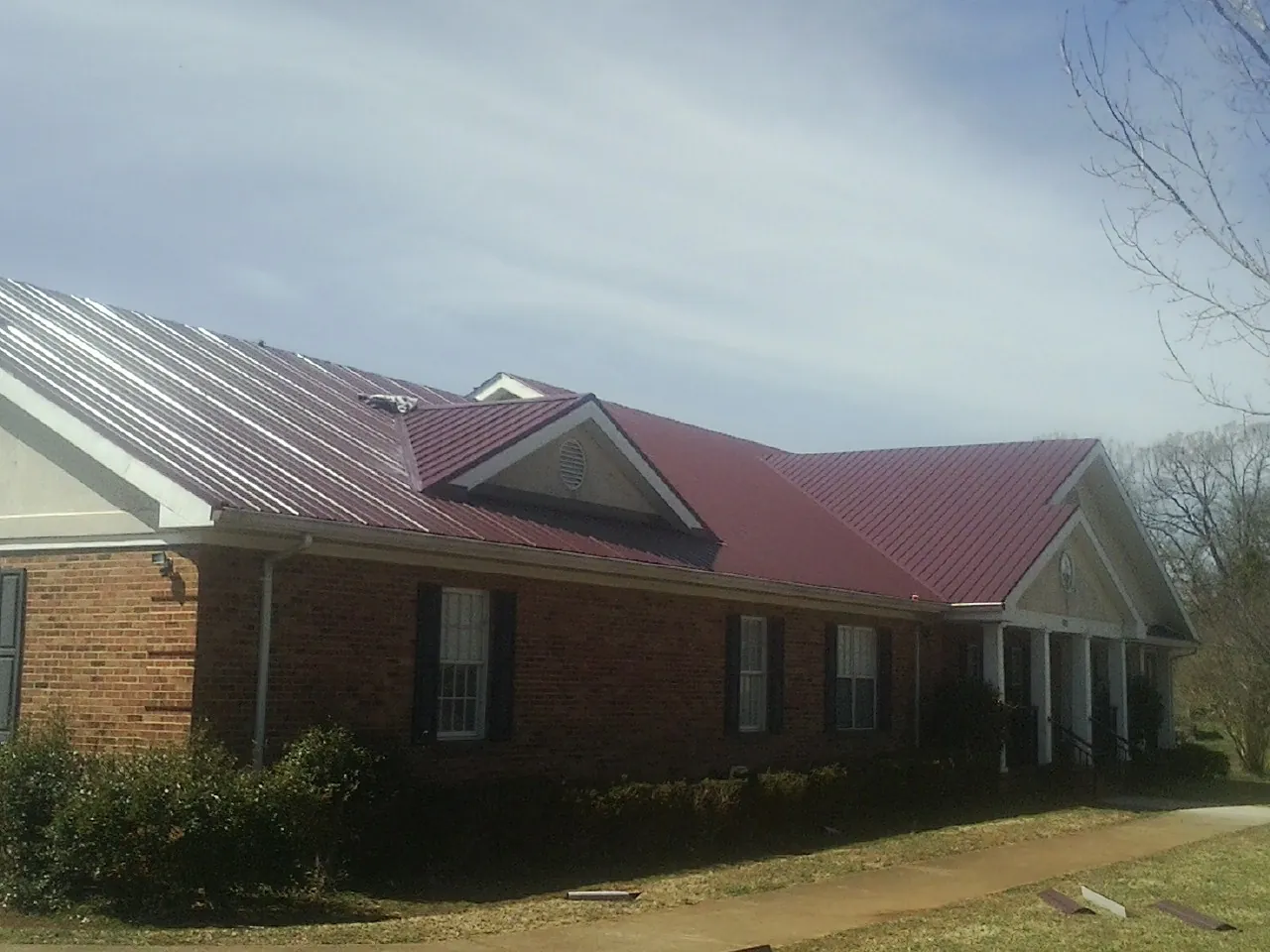 Red metal roof with gabled entries on a long brick building, from a Hail Damage Roof Repair job in Hockley