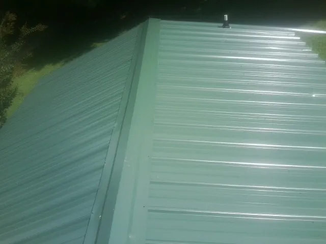 New green metal panels meeting at the ridge of a roof — Flat Roof Repair work by our crew in Hockley