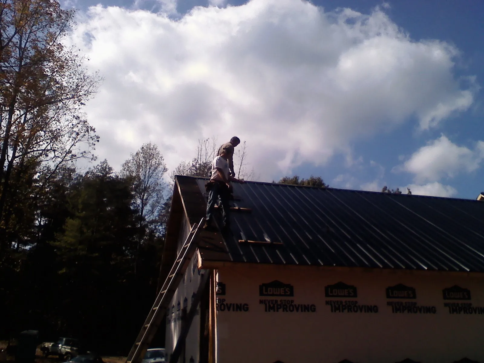 Roofer fastening dark metal panels high against a cloudy sky, from a Roof Inspection job in Hockley