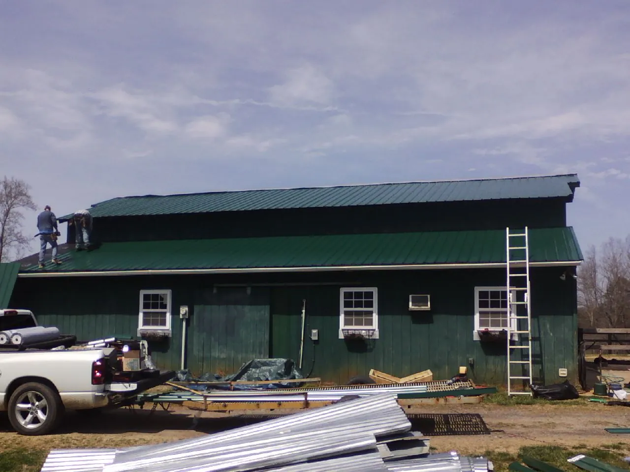 Crew installing green metal roofing on a large green barn in Hockley