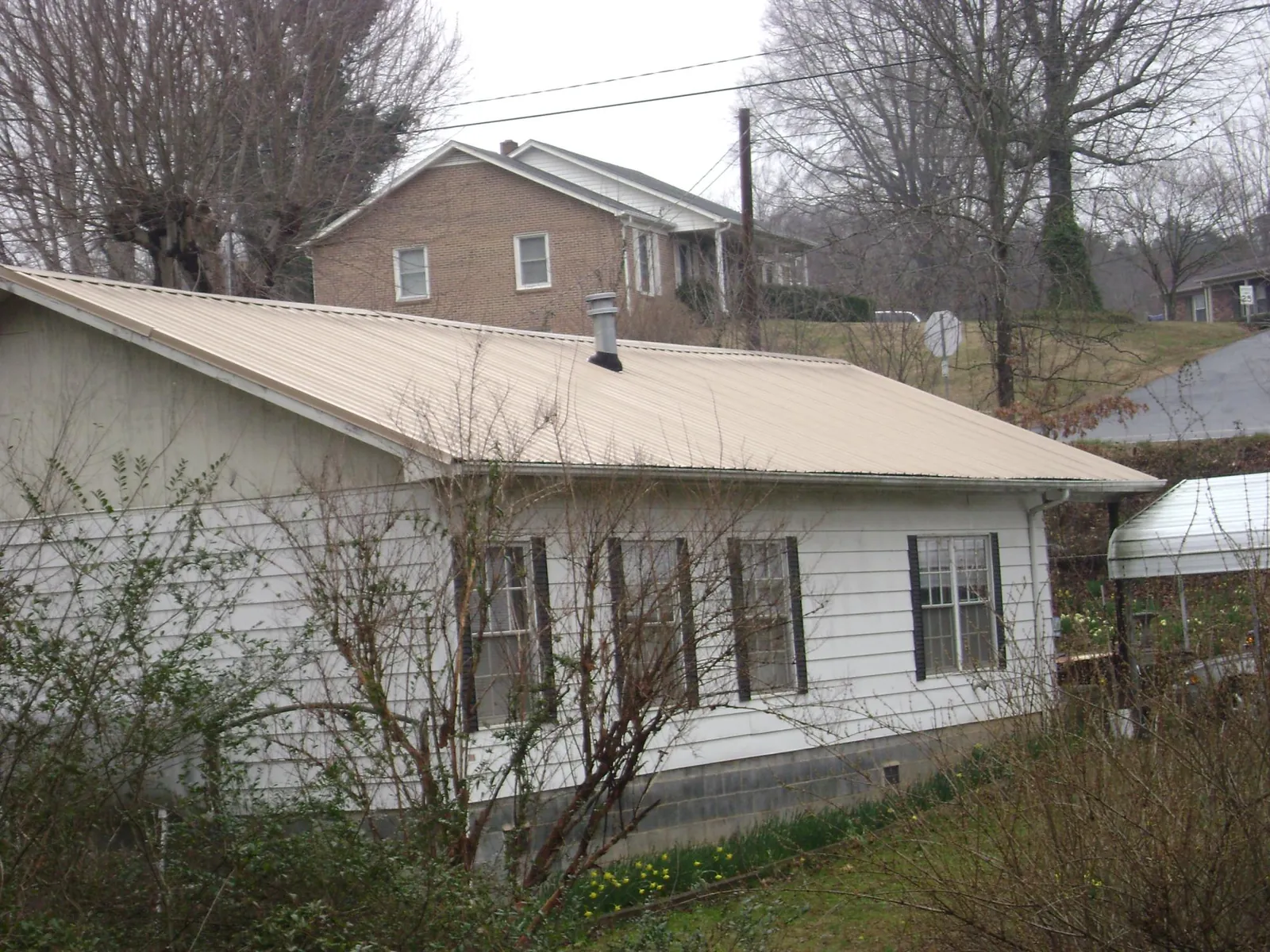 Tan metal roof on a white sided house set into a hillside — Commercial Roofing by Roofing Brothers in Hockley